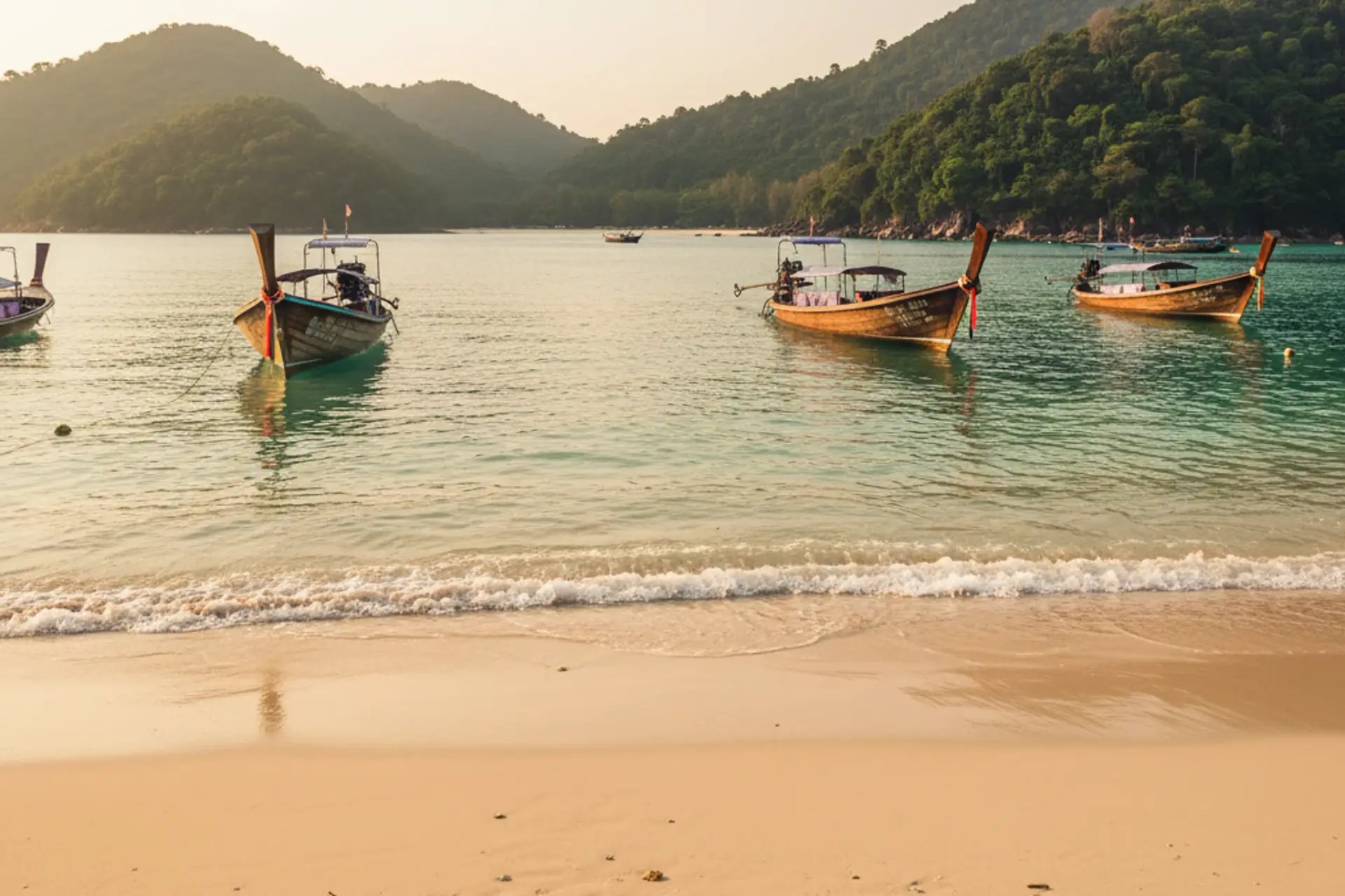 Longtail boats resting on calm, golden water at a Thai beach at sunrise